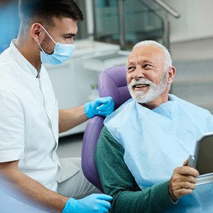Senior patient looking at dentist while holding small mirror