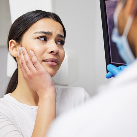 Woman with dentist touching her hand to her jaw in pain