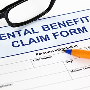 Blue top of dental benefits claim form with black-framed glasses and pen