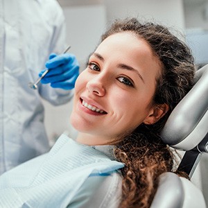 Dentist approaching smiling woman with instrument to perform exam
