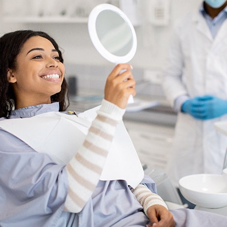 Woman smiling at reflection in handheld mirror
