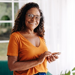 Senior woman with glasses smiling while looking at phone