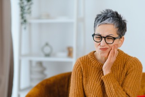 Woman in orange sweater sitting on chair with a toothache